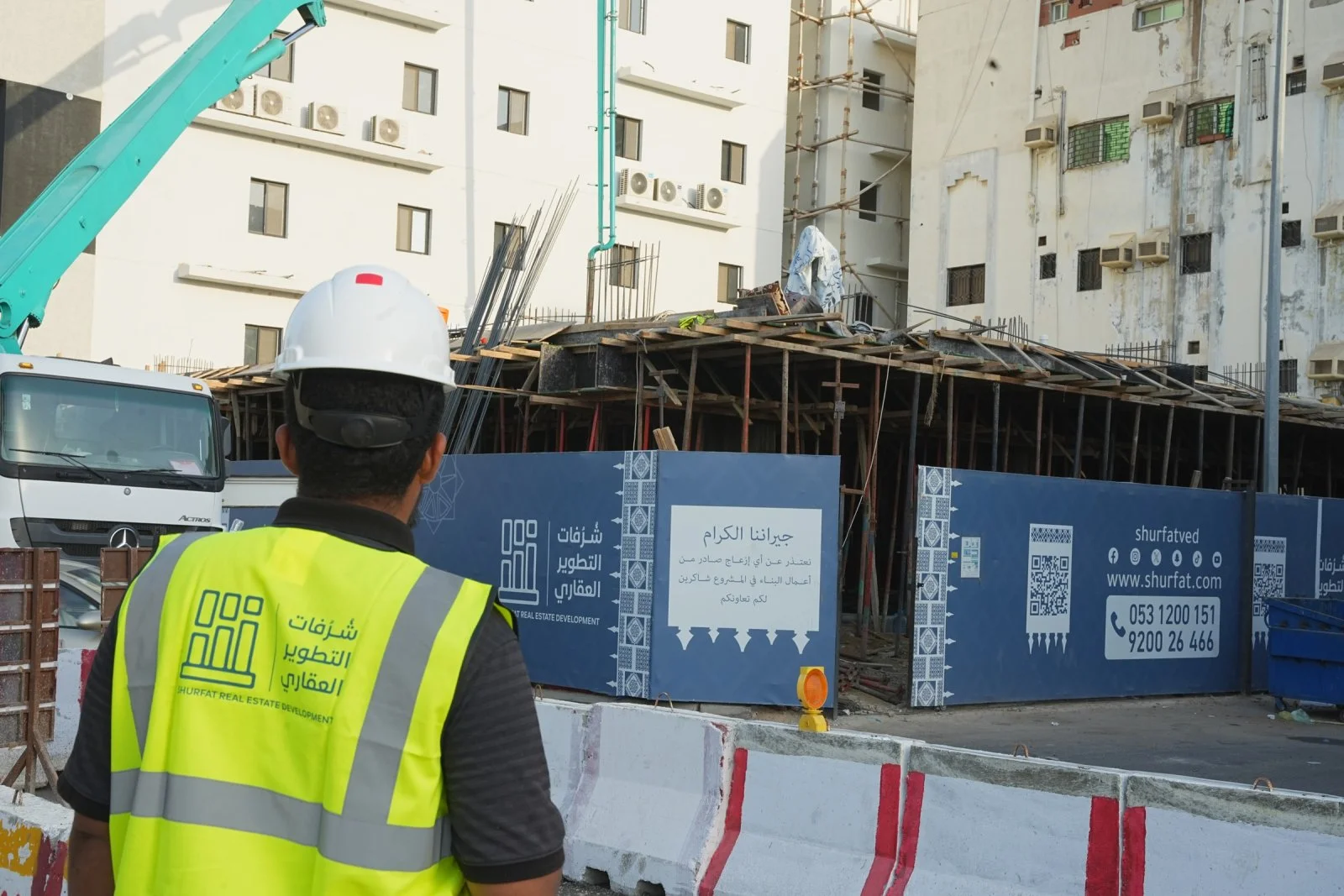 Site photograph, Al-Nuzhah: a Shurfat engineer beside the hoarding that apologises to the neighbours for the building works